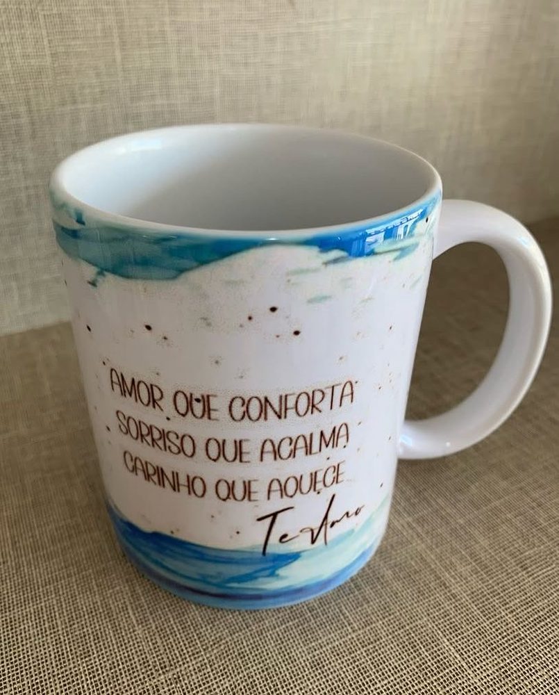 Caneca branca com aquarela azul e a frase Amor que conforta sorriso que acalma carinho que aquece