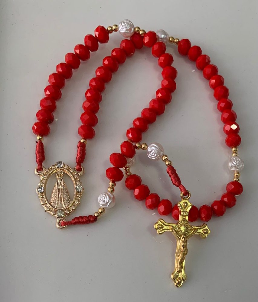 Terço de cristais vermelhos com rosas brancas, medalha dourada de Nossa Senhora Aparecida