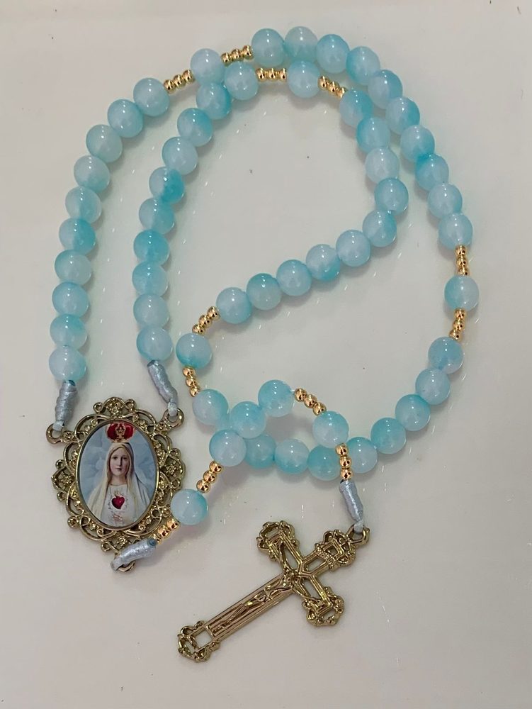 Terço de contas azul-claro com entremeios dourados e medalha de Nossa Senhora de Fátima